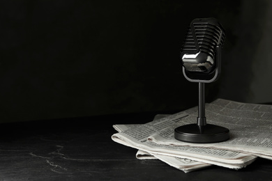 Newspapers and vintage microphone on dark stone table, space for text. Journalist's work