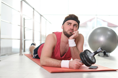 Photo of Lazy young man with abs roller lying on yoga mat indoors