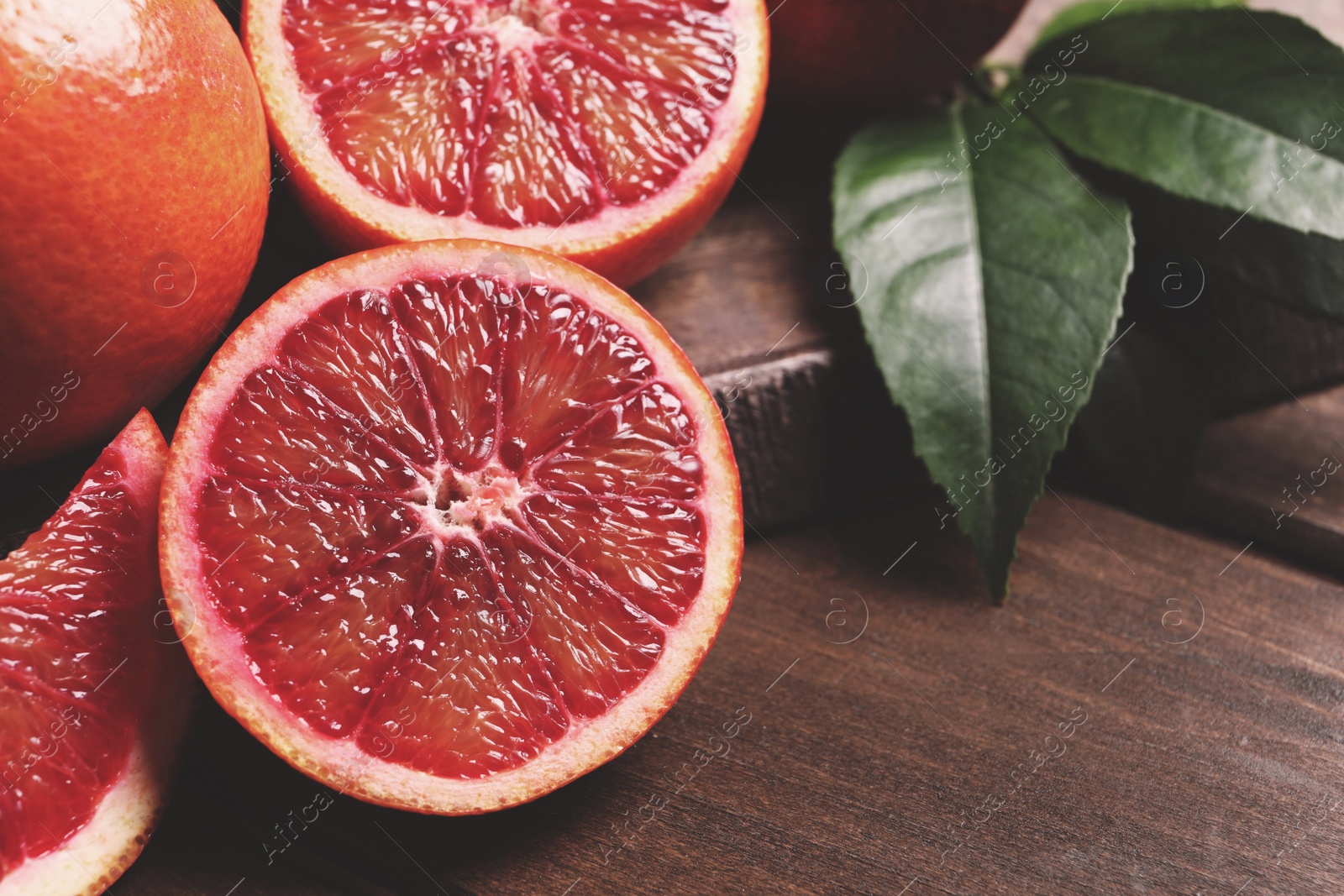 Photo of Cut ripe red oranges and green leaves on wooden table, closeup