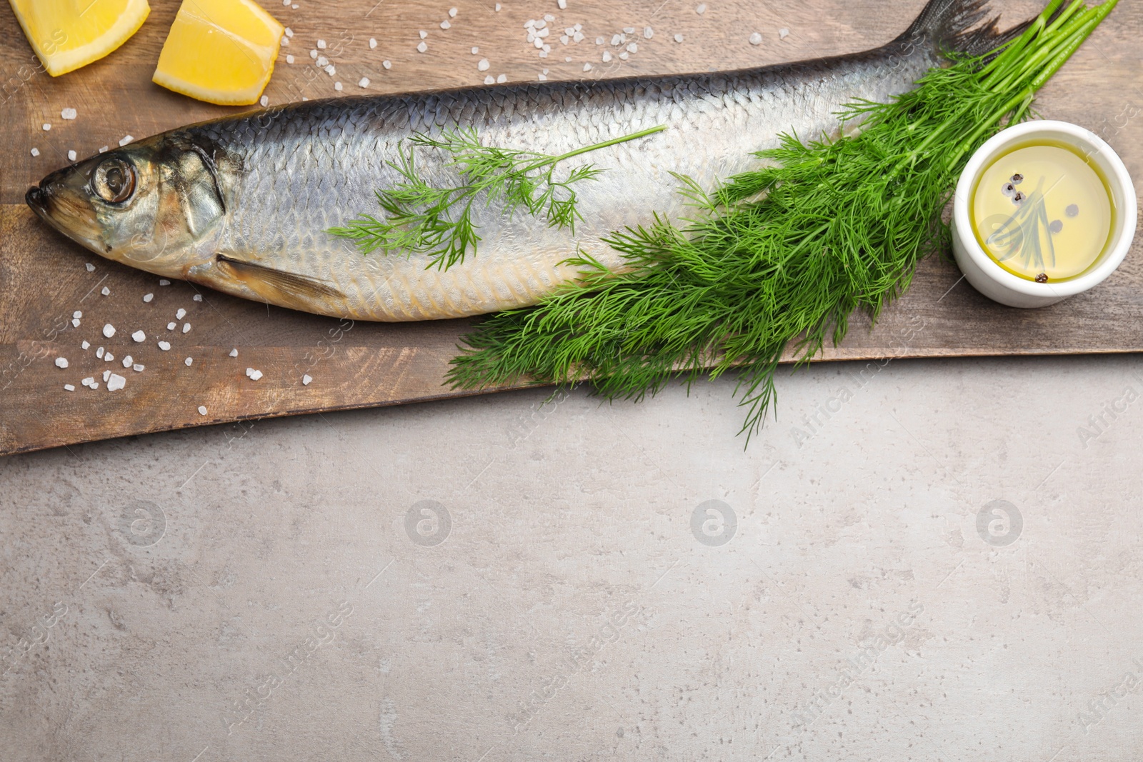 Photo of Board with delicious salted herring, dill, lemon and olive oil on grey table, flat lay. Space for text