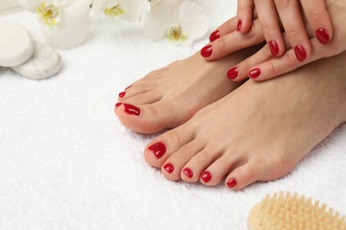 Photo of Woman showing stylish toenails after pedicure procedure and manicured hands with red polish on white terry towel, closeup. Space for text