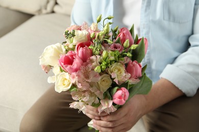 Photo of Man holding bouquet of beautiful flowers indoors, closeup