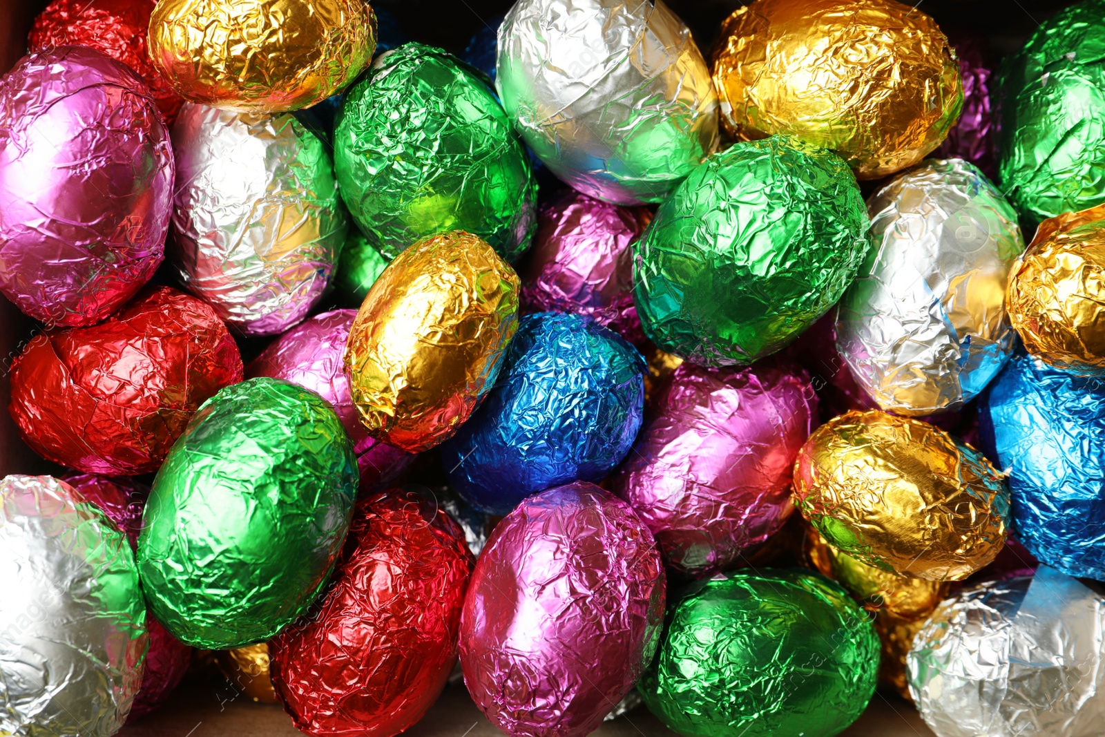 Photo of Chocolate eggs wrapped in colorful foil as background, top view