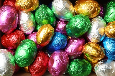 Chocolate eggs wrapped in colorful foil as background, top view