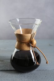 Photo of Glass chemex coffeemaker with tasty drip coffee on grey wooden table