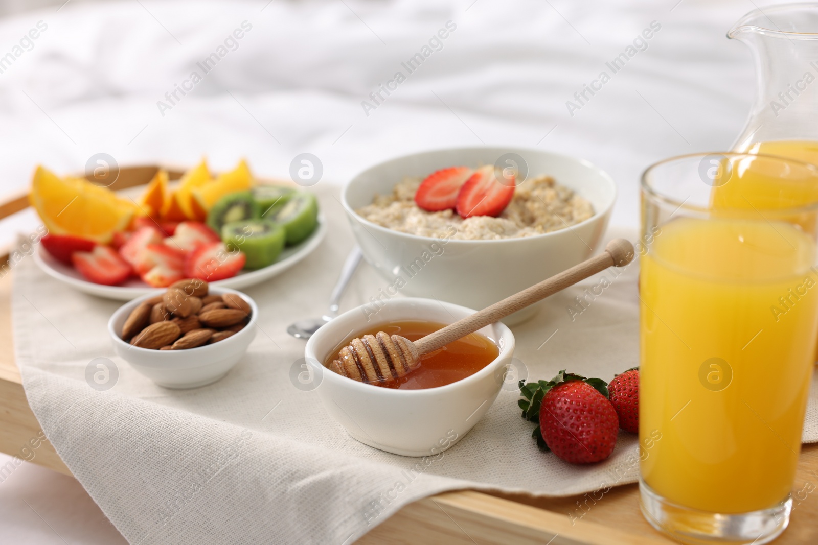 Tasty breakfast served in bed. Oatmeal, juice, fruits, almonds and honey on wooden tray, closeup Photo of Tasty breakfast served in bed. Oatmeal, juice, fruits, almonds and honey on wooden tray, closeup
