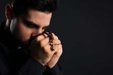 Photo of Priest with rosary beads praying on black background, closeup. Space for text