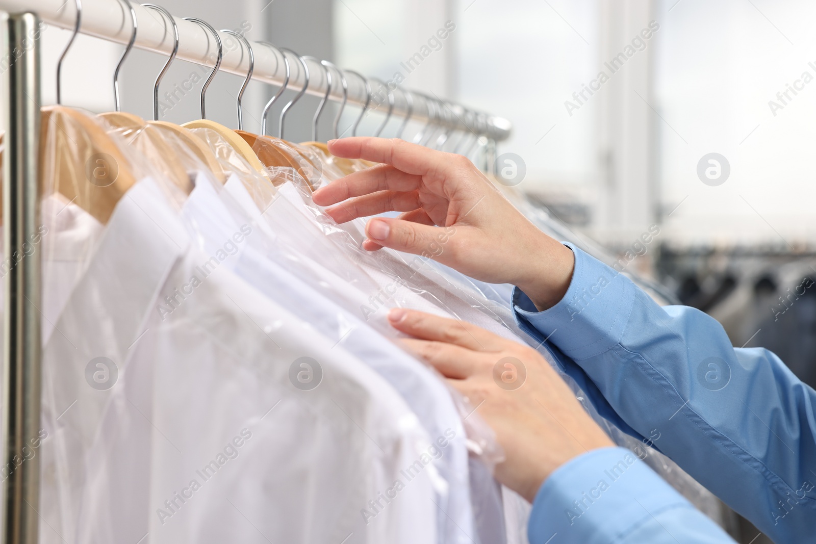 Photo of Dry-cleaning service. Woman taking shirt in plastic bag from rack indoors, closeup