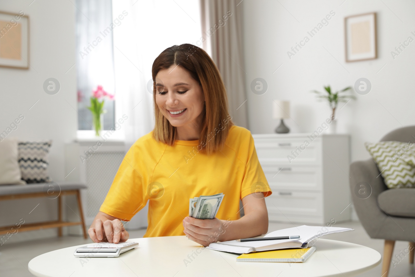 Photo of Smiling woman counting money at table indoors