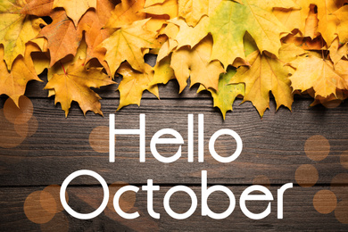 Text Hello October and autumn leaves on wooden background with blurred lights, top view