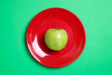 Red plate with ripe juicy apple on green background, top view