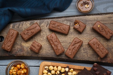 Photo of Delicious chocolate candy bars with caramel and nuts on grey wooden table, flat lay