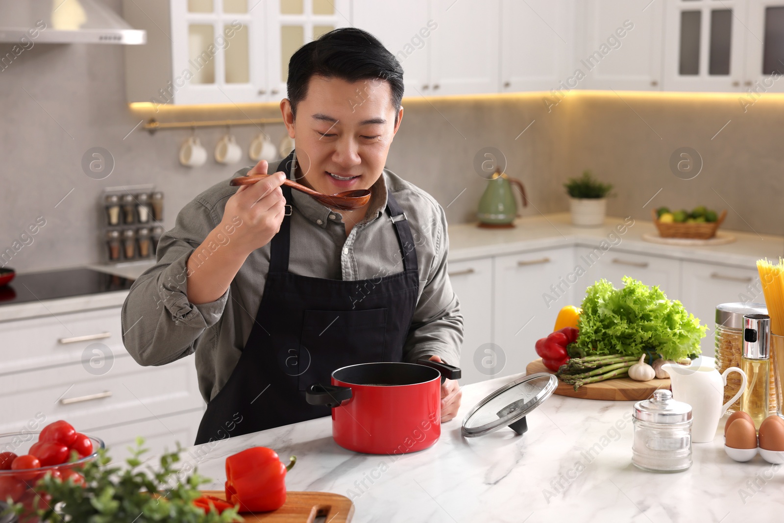 Photo of Cooking process. Man tasting dish at countertop in kitchen