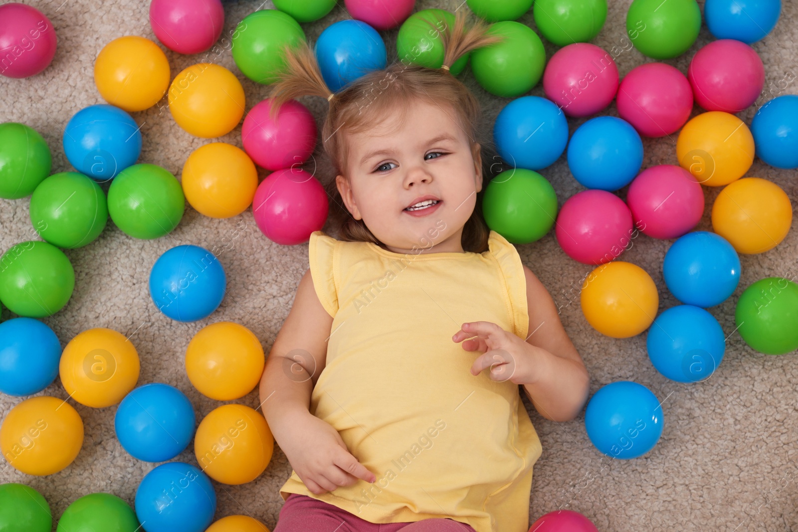Photo of Cute little child playing with balls on floor, top view