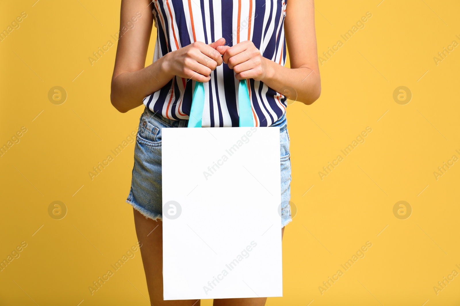 Photo of Young woman with paper bag on yellow background, closeup