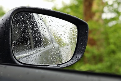 Closeup of car side rear view mirror with rain drops