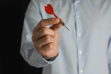 Photo of Man holding red dart on black background, closeup. Space for text