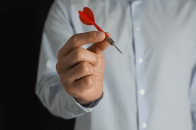 Man holding red dart on black background, closeup. Space for text