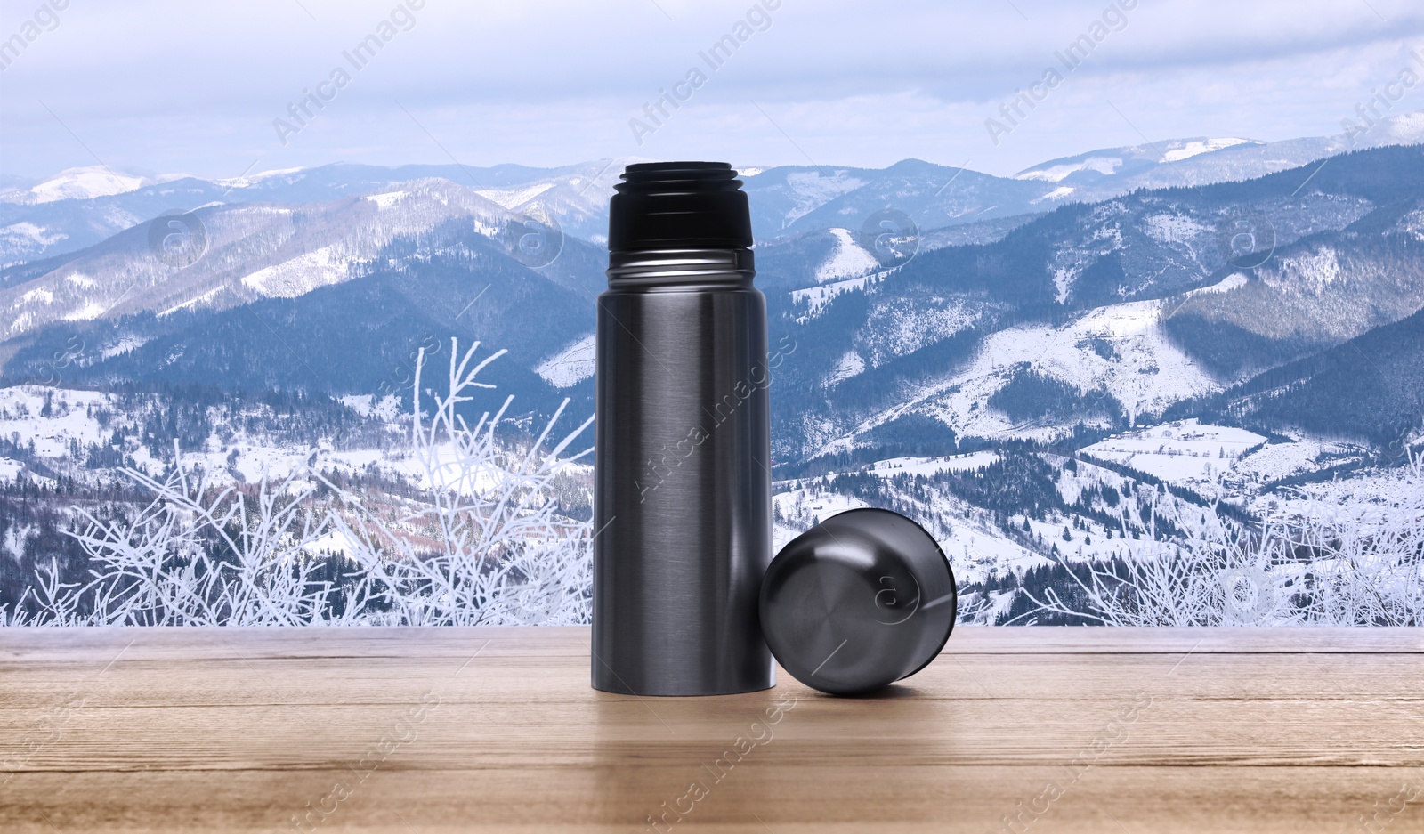 Image of Wooden desk with thermos and mountain landscape on background
