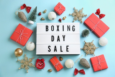 Photo of Lightbox with phrase BOXING DAY SALE and Christmas decorations on light blue background, flat lay