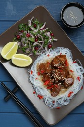 Pieces of soy sauce chicken with noodle, salad and lime served on blue wooden table, flat lay