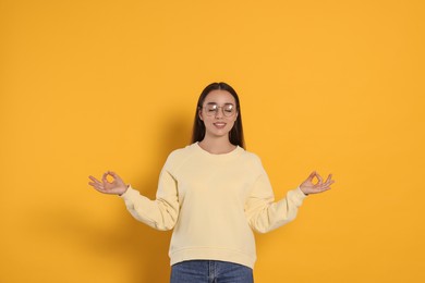 Find zen. Beautiful young woman meditating on yellow background