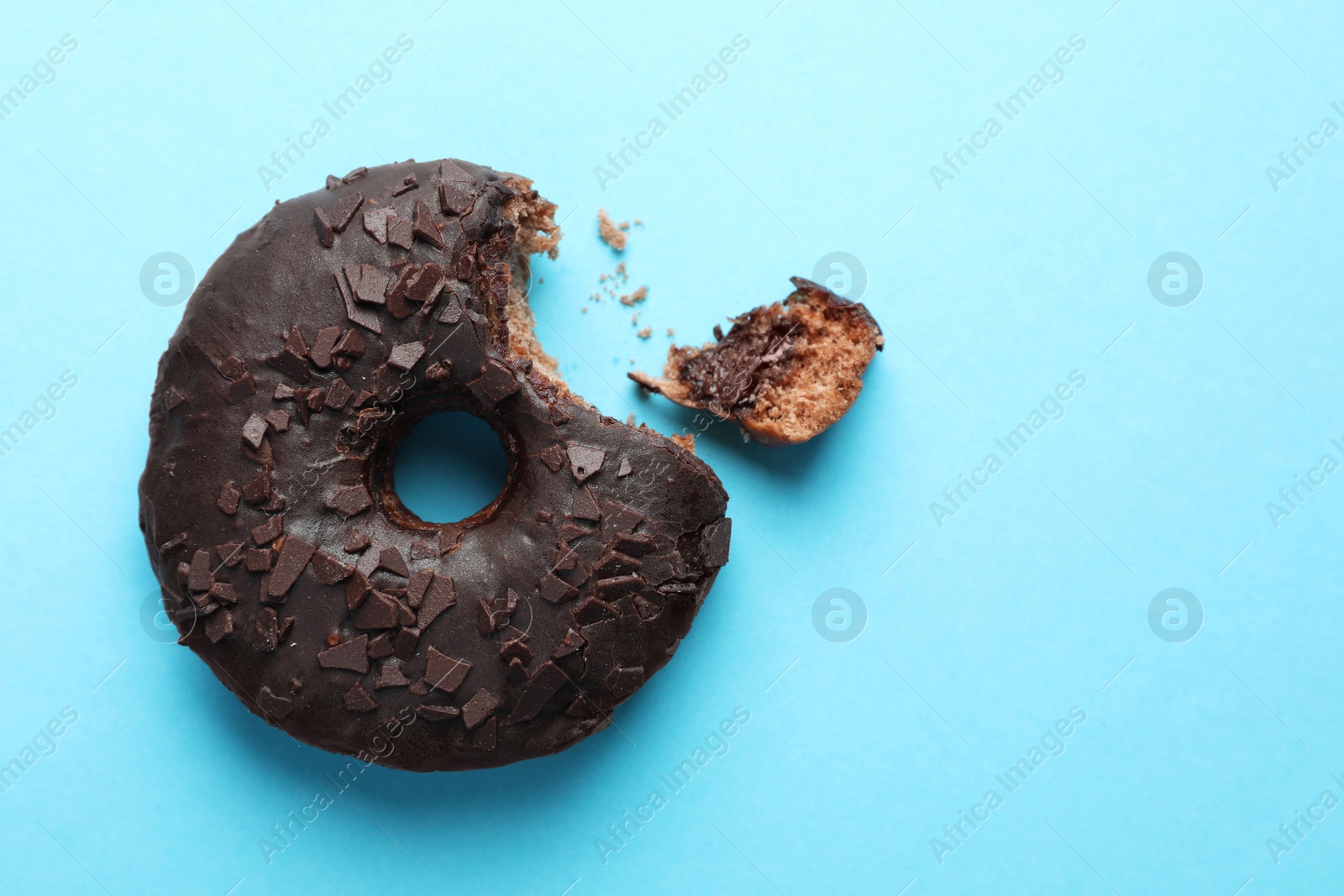 Photo of Sweet bitten glazed donut decorated with chocolate on light blue background, top view. Space for text