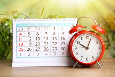 Calendar and alarm clock on wooden table against blurred green background