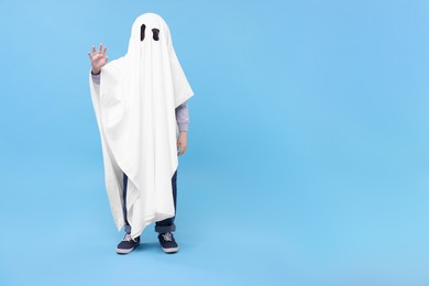 Photo of Child in white ghost costume on light blue background, space for text. Halloween celebration