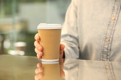 Woman holding takeaway paper cup at table, closeup. Coffee to go