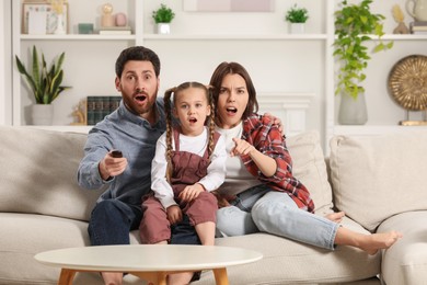 Surprised family watching TV on sofa at home