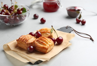 Photo of Fresh delicious puff pastry with sweet cherries served on light table