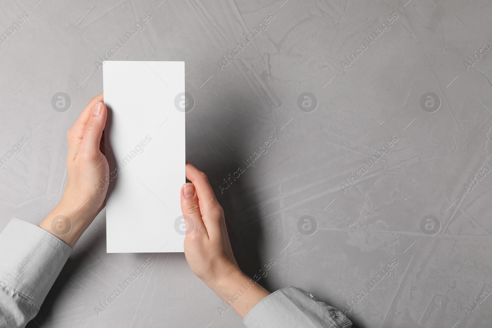 Photo of Woman holding blank card at light grey table, top view. Mockup for design