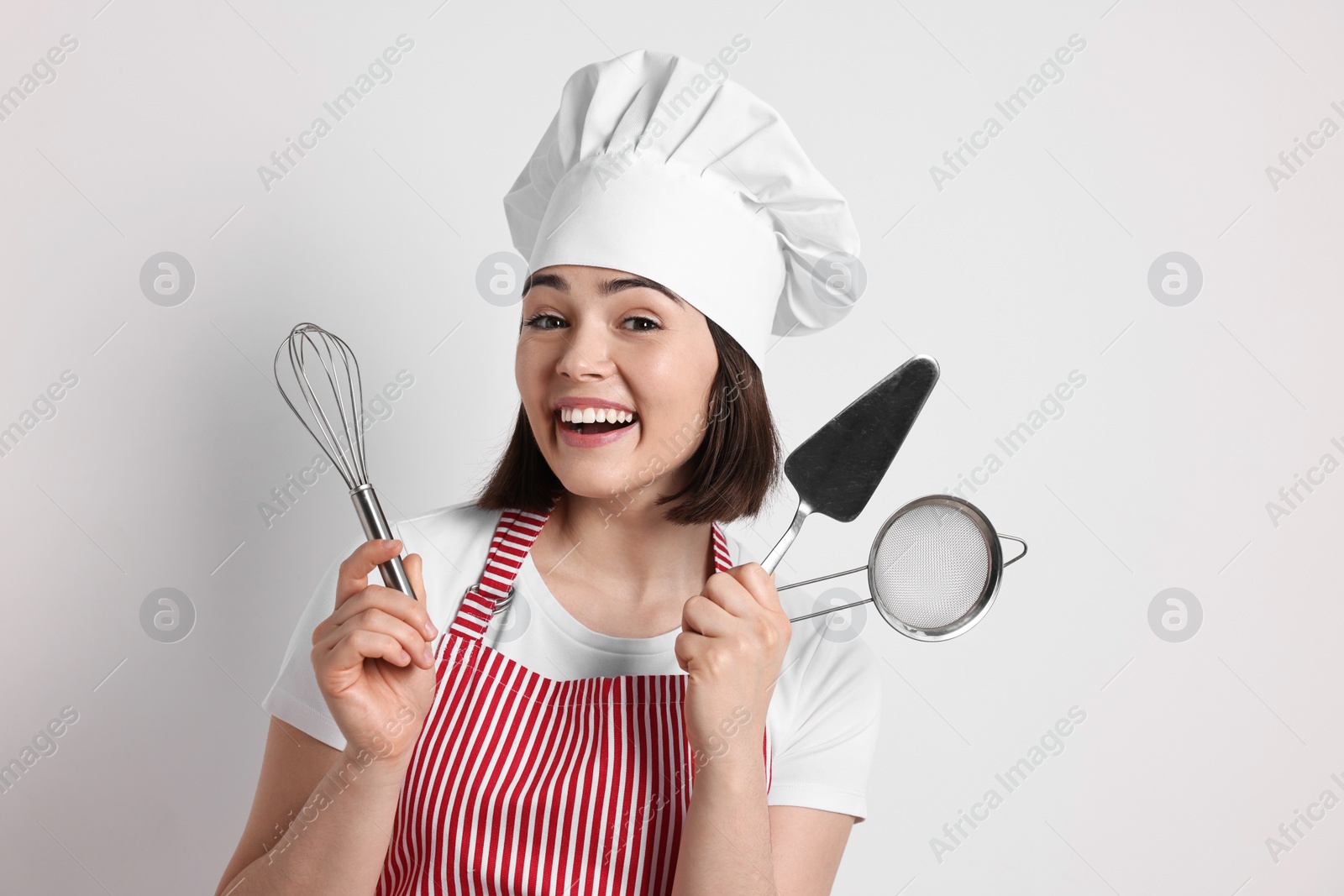 Photo of Happy confectioner holding professional tools on light grey background