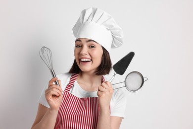 Happy confectioner holding professional tools on light grey background