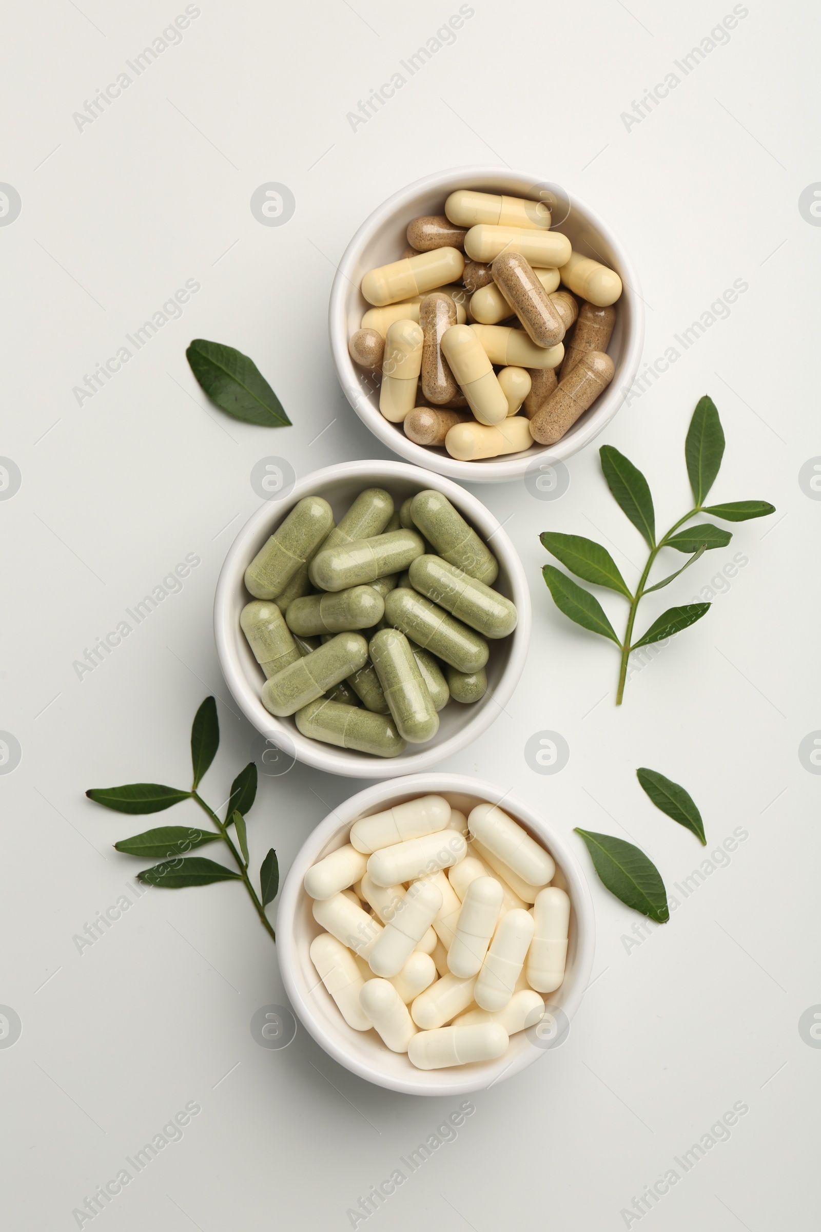 Photo of Different vitamin capsules in bowls and leaves on white background, flat lay