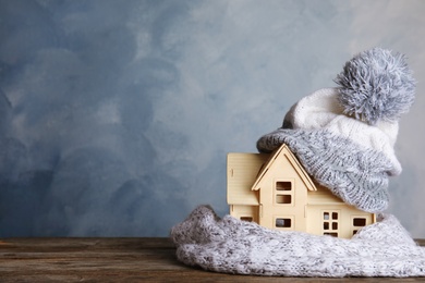 Photo of Plywood toy house with warm hat, scarf and space for text against color background. Heating system
