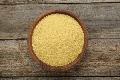 Photo of Bowl of raw couscous on wooden table, top view