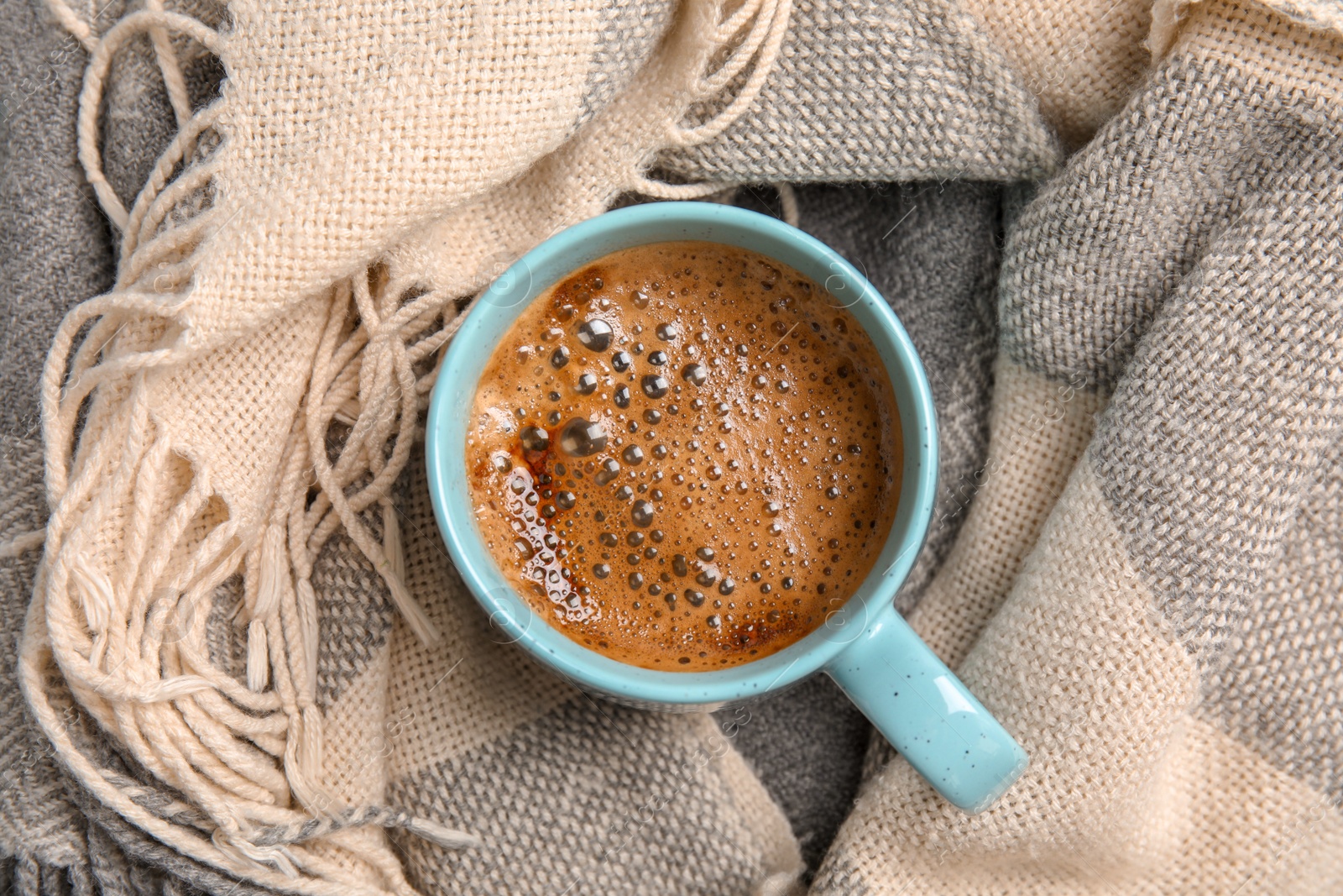 Photo of Cup of hot winter drink on warm scarf. Cozy season