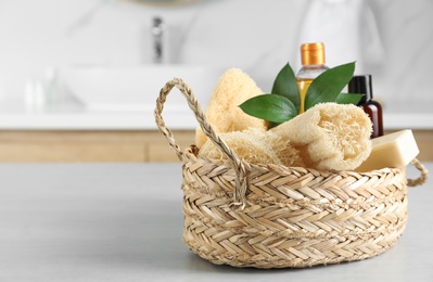 Photo of Natural loofah sponges in wicker basket on table indoors. Space for text