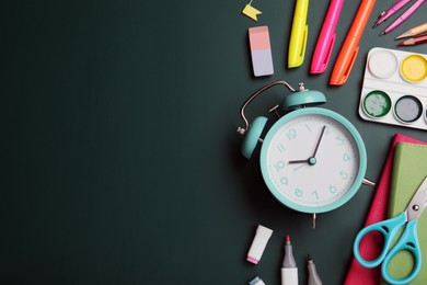 Flat lay composition with alarm clock and different stationery on green chalkboard, space for text. School time