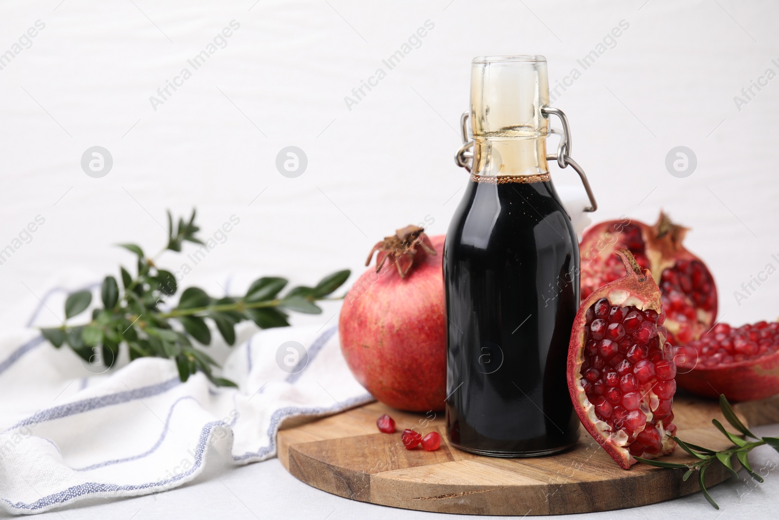 Photo of Tasty pomegranate sauce in bottle, branches and fruits on light table, closeup. Space for text