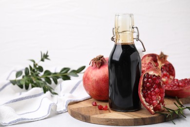 Tasty pomegranate sauce in bottle, branches and fruits on light table, closeup. Space for text