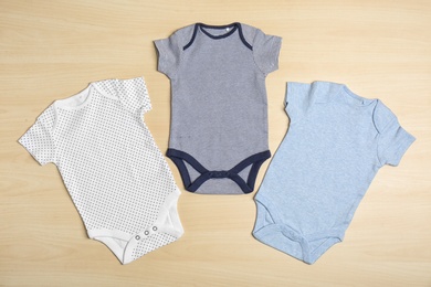 Photo of Different baby bodysuits on wooden background, top view