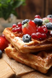 Photo of Delicious Belgian waffles, berries and powdered sugar on wooden board, closeup