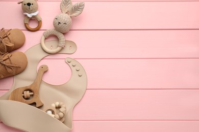 Flat lay composition with silicone baby bib, toys and accessories on pink wooden background. Space for text