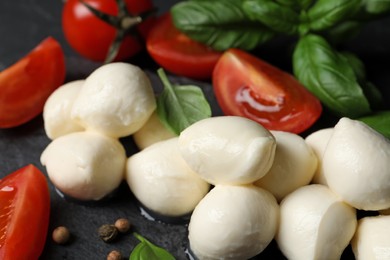 Photo of Delicious mozzarella balls, tomatoes and basil leaves on black table, closeup