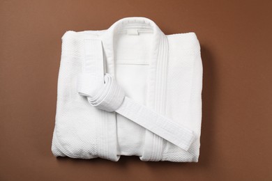 Photo of White karate belt and kimono on brown background, top view