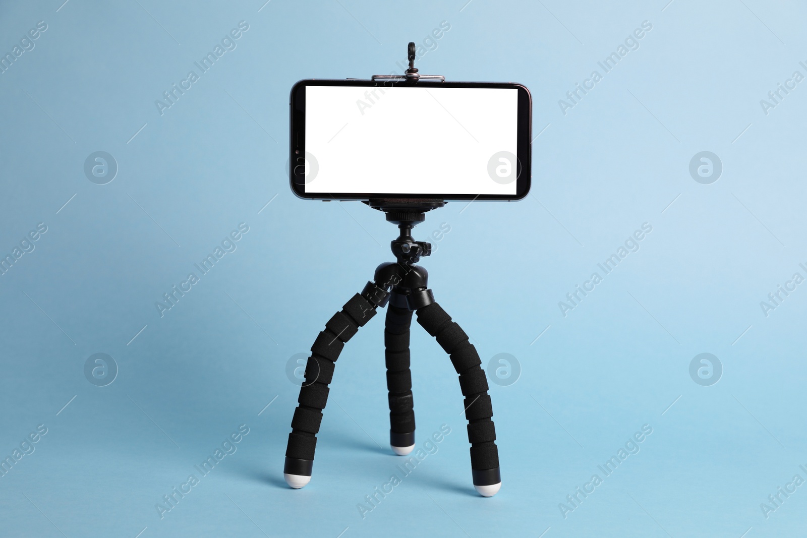 Photo of Modern tripod with smartphone on light blue background