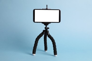 Photo of Modern tripod with smartphone on light blue background